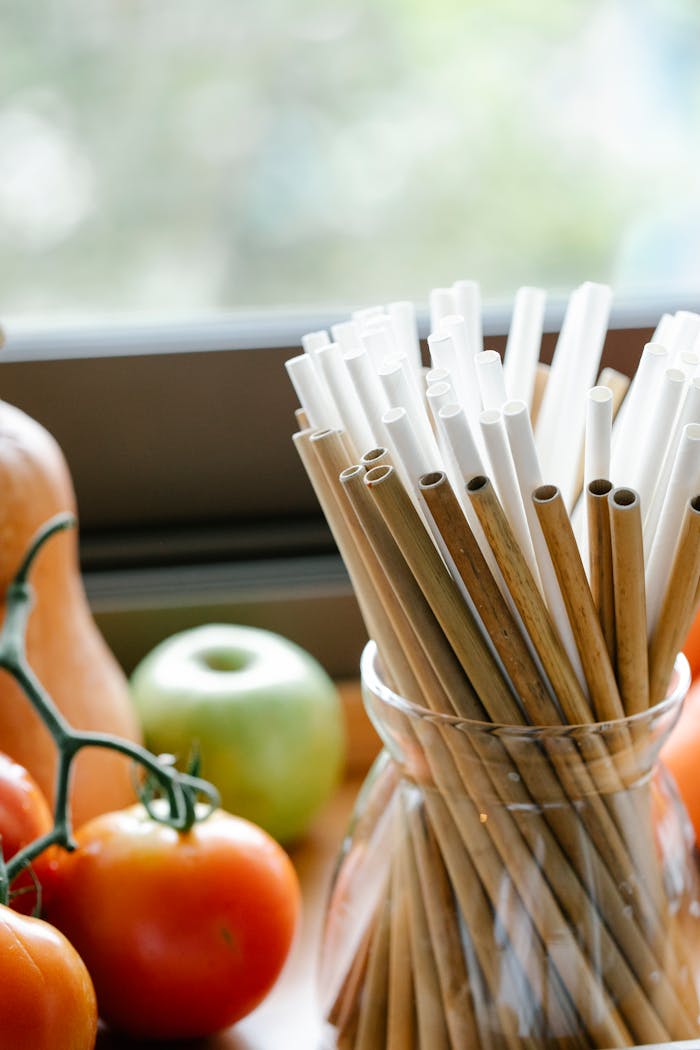 Composition of reusable bamboo straws in glass jar placed on table near organic tomatoes and apple