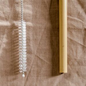 Close-up of a bamboo straw and a reusable cleaning brush on a linen cloth.