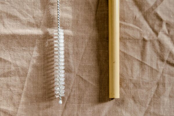 Close-up of a bamboo straw and a reusable cleaning brush on a linen cloth.